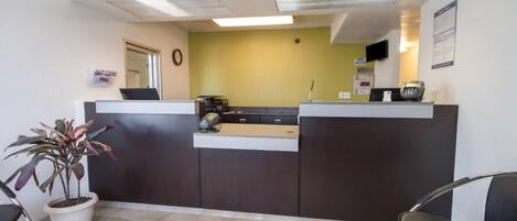 A reception area with a desk, a plant, a clock, and a wall-mounted phone.