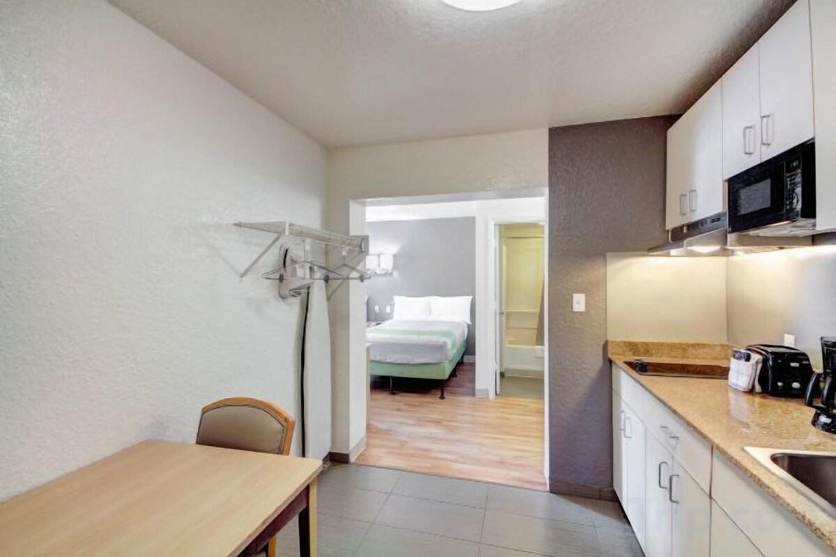 A compact kitchen with a microwave, a sink, and a dining area with a chair.