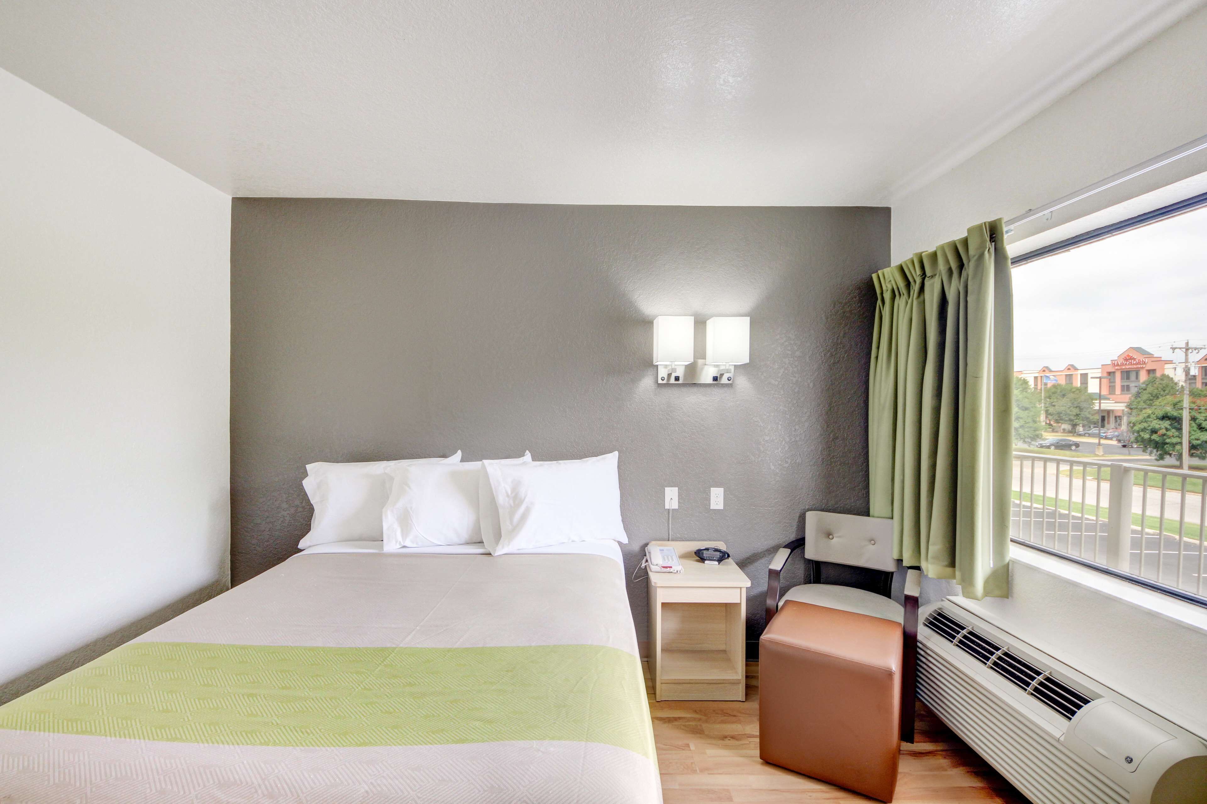 Ein Hotelzimmer mit Bett, Nachttisch, Lampe und Blick ins Freie.