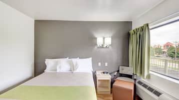 A hotel room with a bed, bedside table, lamp, and a view of the outside.