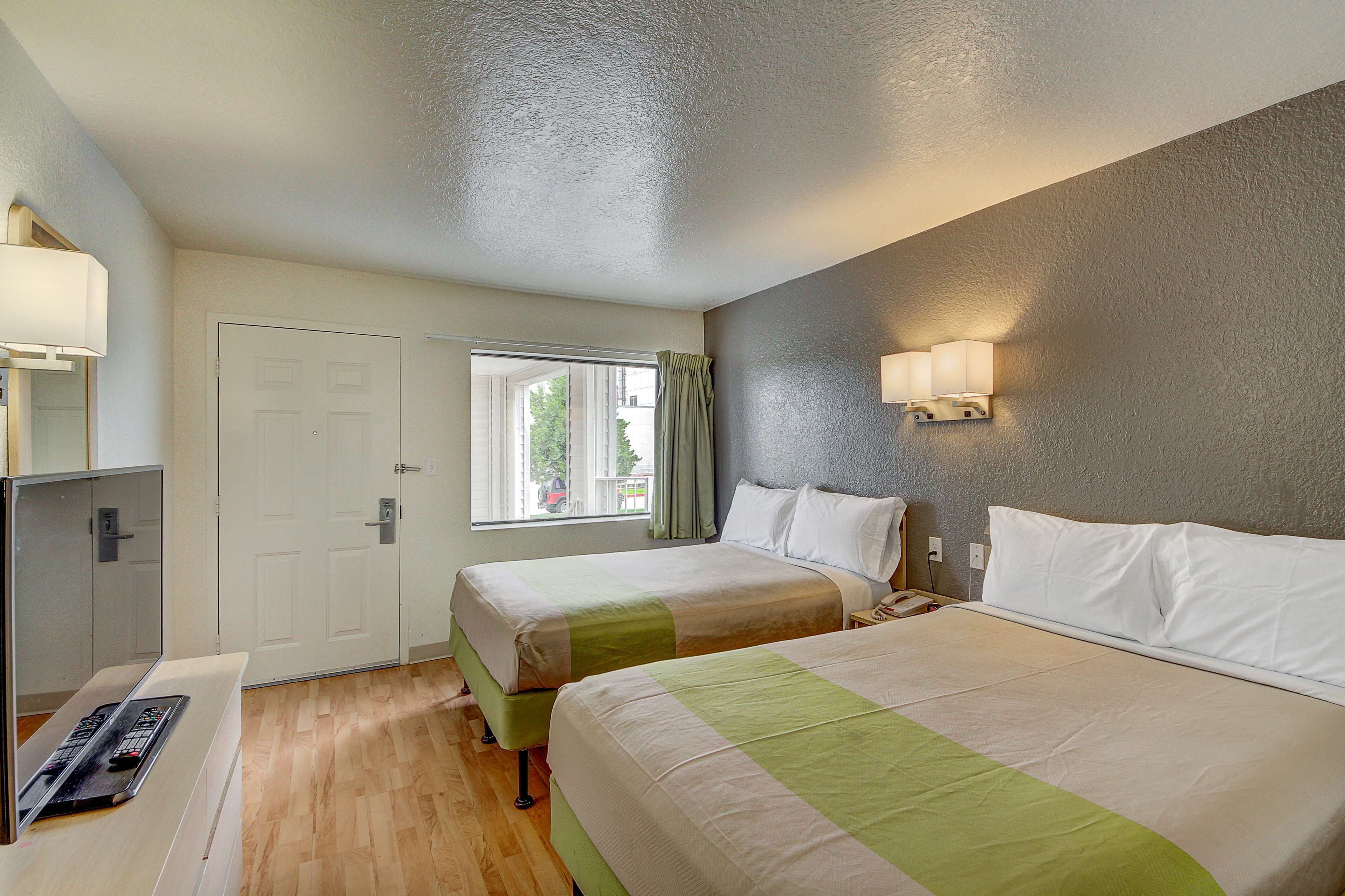 Une chambre d’hôtel avec deux lits, une fenêtre avec des rideaux, une lampe de chevet et un bureau avec une télécommande.
