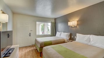 A hotel room with two beds, a window with curtains, a bedside lamp, and a desk with a remote control.