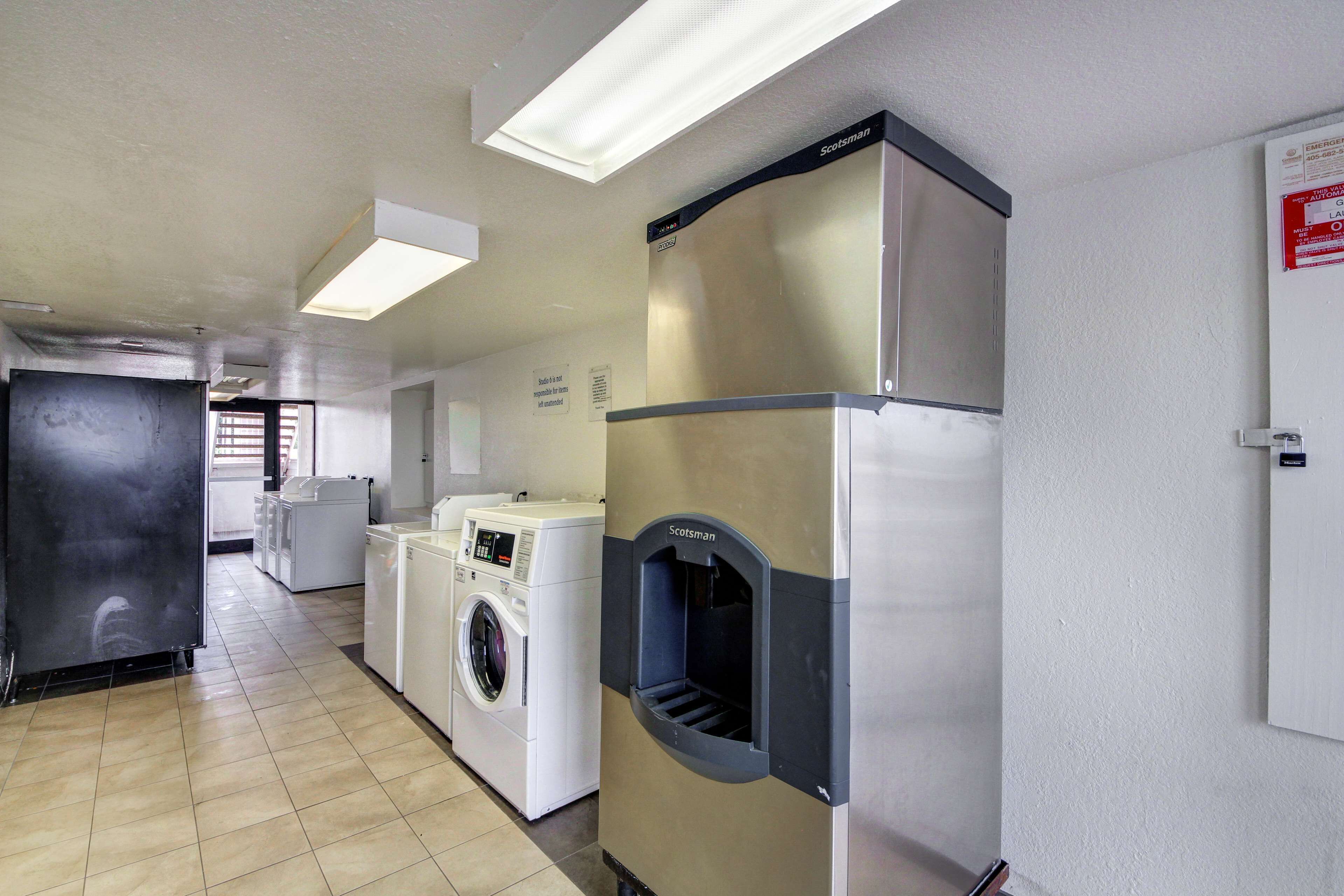 A laundry room with a front-loading washer and dryer, a stainless steel Scissorsman water fountain, and a white door with a red emergency exit sign.