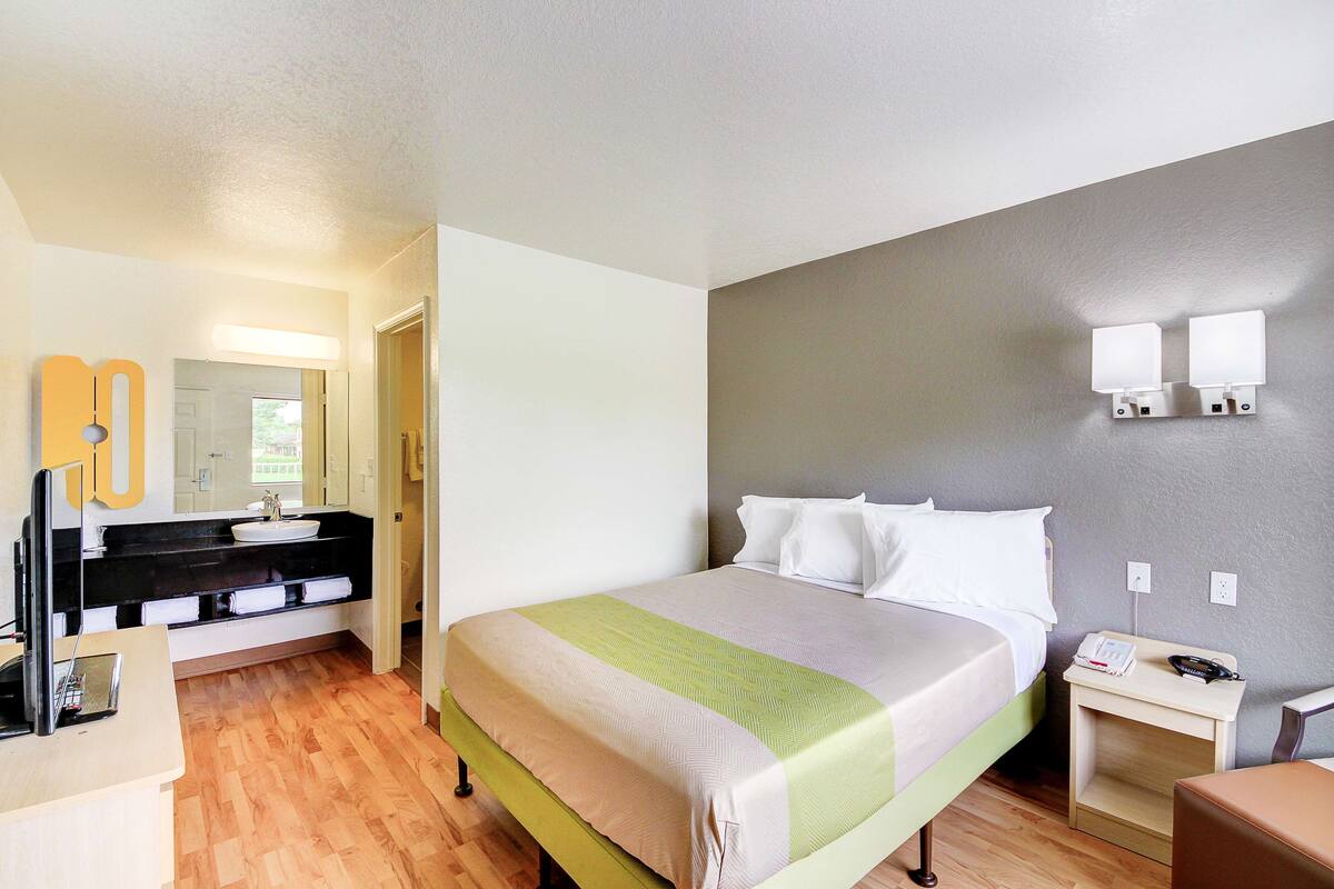 A hotel room with a bed, bedside table, and a bathroom with a sink and mirror.