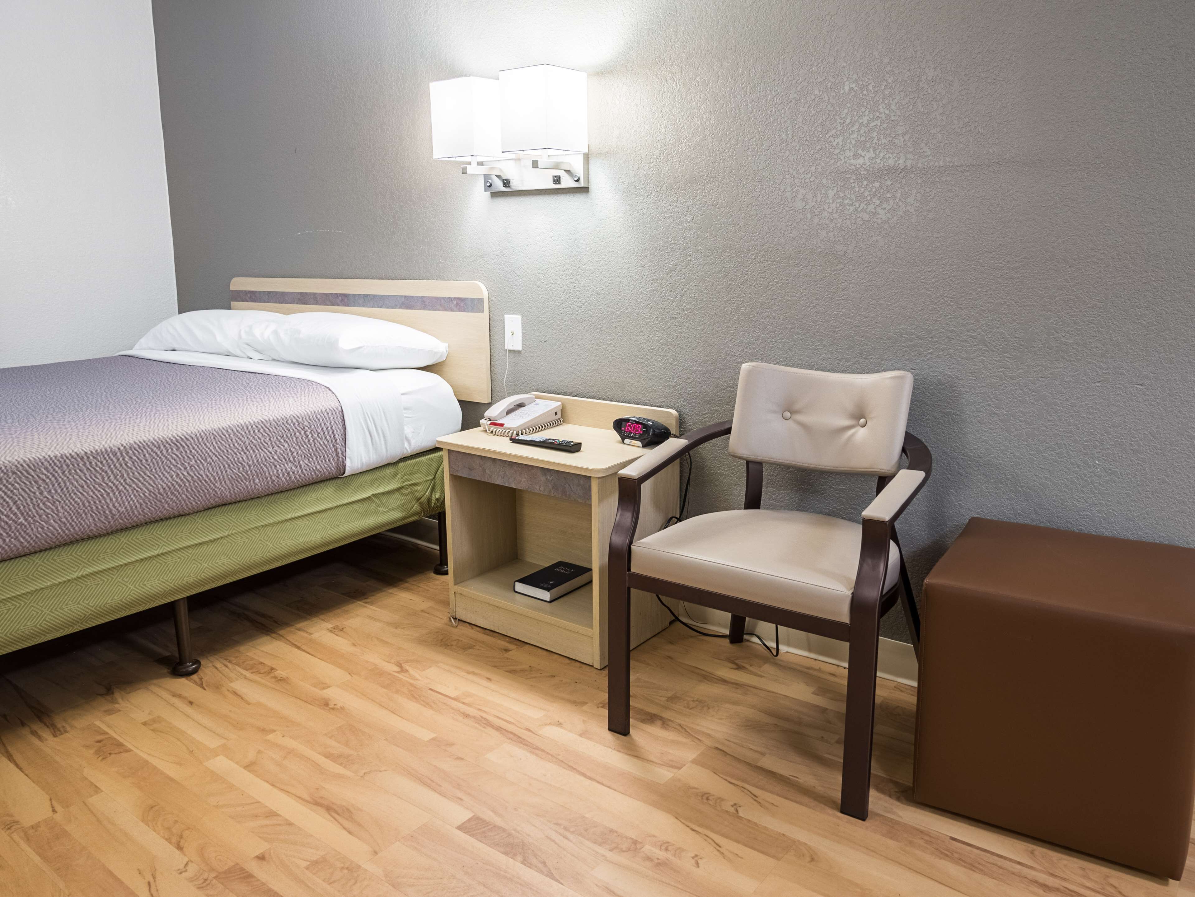Ein Hotelzimmer mit einem Bett, einem Schreibtisch mit Telefon und Buch, einem Sessel und einem braunen Hocker.