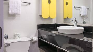 Une salle de bain moderne avec des toilettes, un lavabo et un miroir. On trouve des serviettes sur le porte-serviettes et un rouleau de papier toilette accroché au mur.
