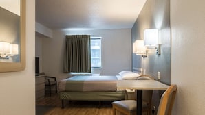 Habitación de hotel compacta con cama, escritorio, silla y ventana con cortinas.