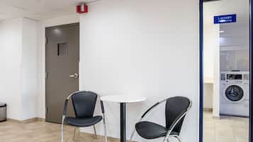 A hotel room with a door, two chairs, a small table, and a laundry area with a washing machine.