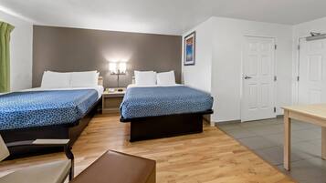 A hotel room with two beds, a desk, a chair, and a door.