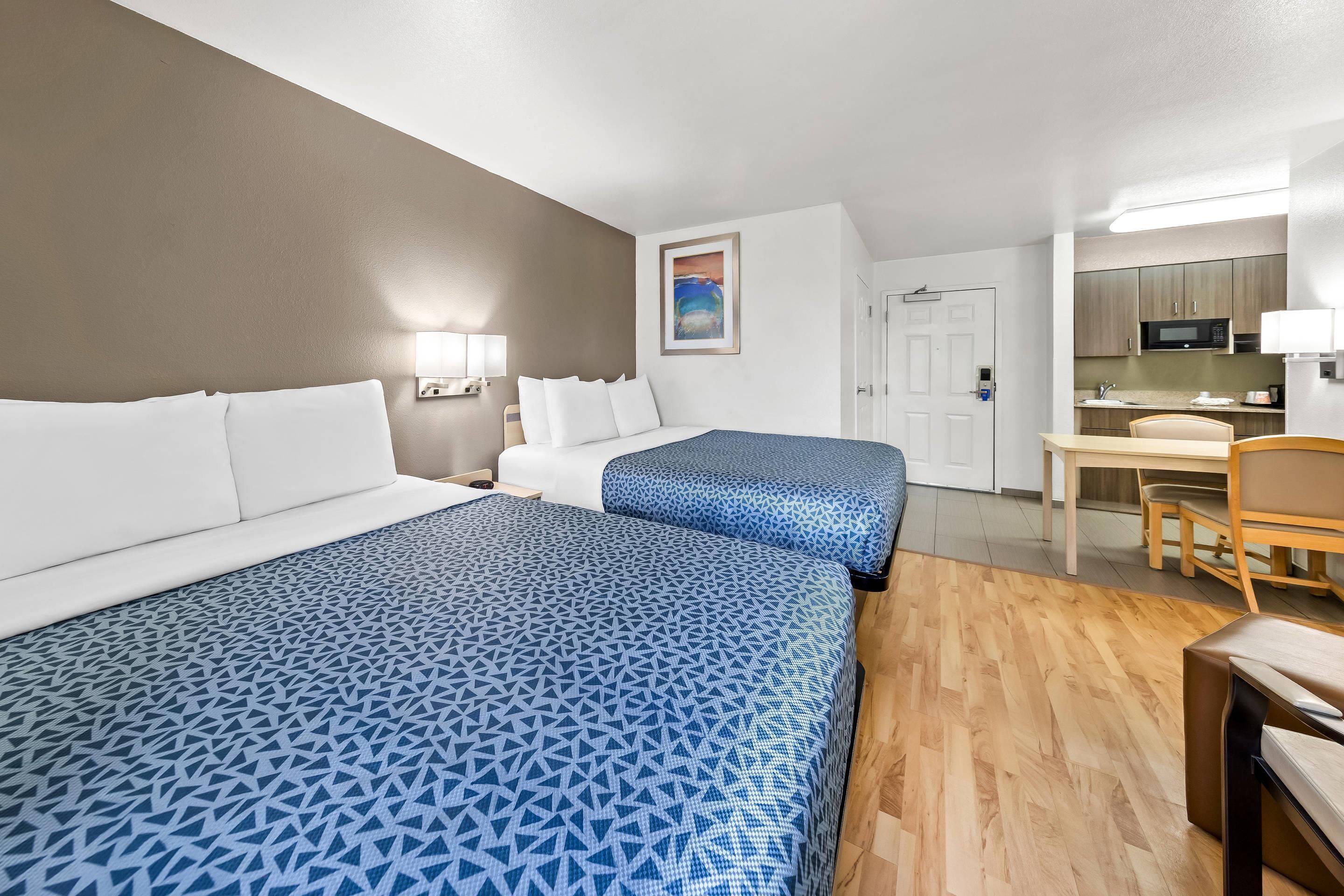 A hotel room with two beds, a desk, a chair, a microwave, and a small kitchenette.