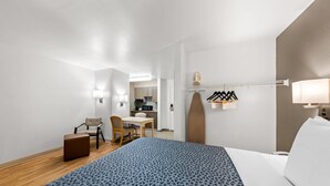 A hotel room with a bed, a desk, a chair, a small table, and a kitchenette. - Suburban Studios Fishers Indianapolis (Fishers)