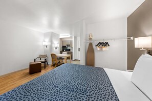A hotel room with a bed, a desk, a chair, a small table, and a kitchenette.