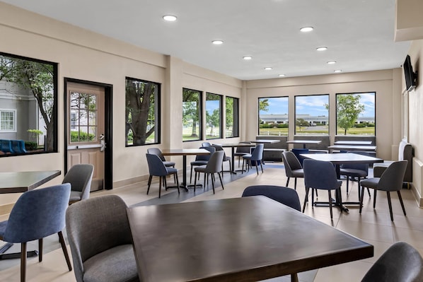 A modern dining area with multiple tables and chairs, large windows offering views of the outdoors, and a clean, minimalist design.
