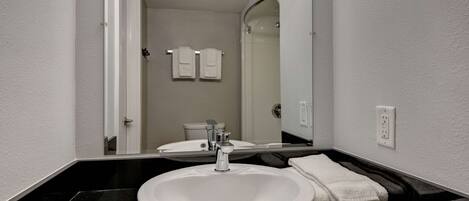 A bathroom with a white sink, black countertop, and a mirror reflecting the toilet and towel rack.