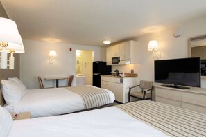 A hotel room with two beds, a kitchenette, a TV, and a desk with a chair. - Suburban Studios Mentor - Cleveland Northeast (Mentor)
