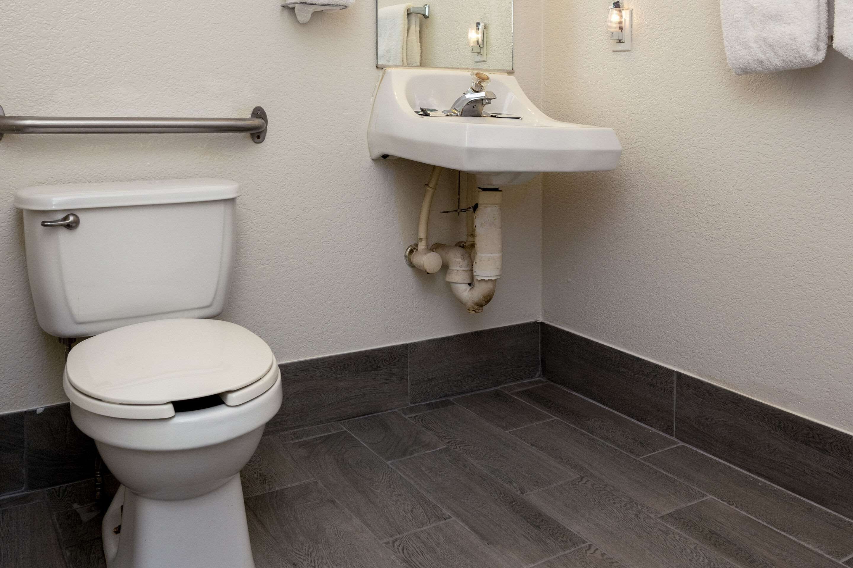 A bathroom with a white toilet, a sink, and a handrail.
