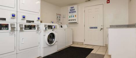 A laundry room with stacked washers and dryers, a black mat, and a door labeled "Employees Only".