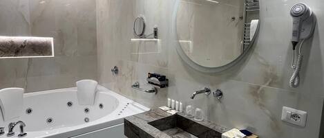 A modern bathroom with a freestanding bathtub, a vanity with a marble countertop, a large mirror, and a hairdryer mounted on the wall.