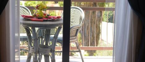 A balcony with a table set for dining, featuring a wicker chair and a red tablecloth.