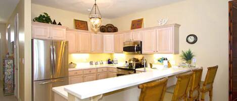 A kitchen with white cabinets, a stainless steel refrigerator, a microwave, and a dining area with four chairs.
