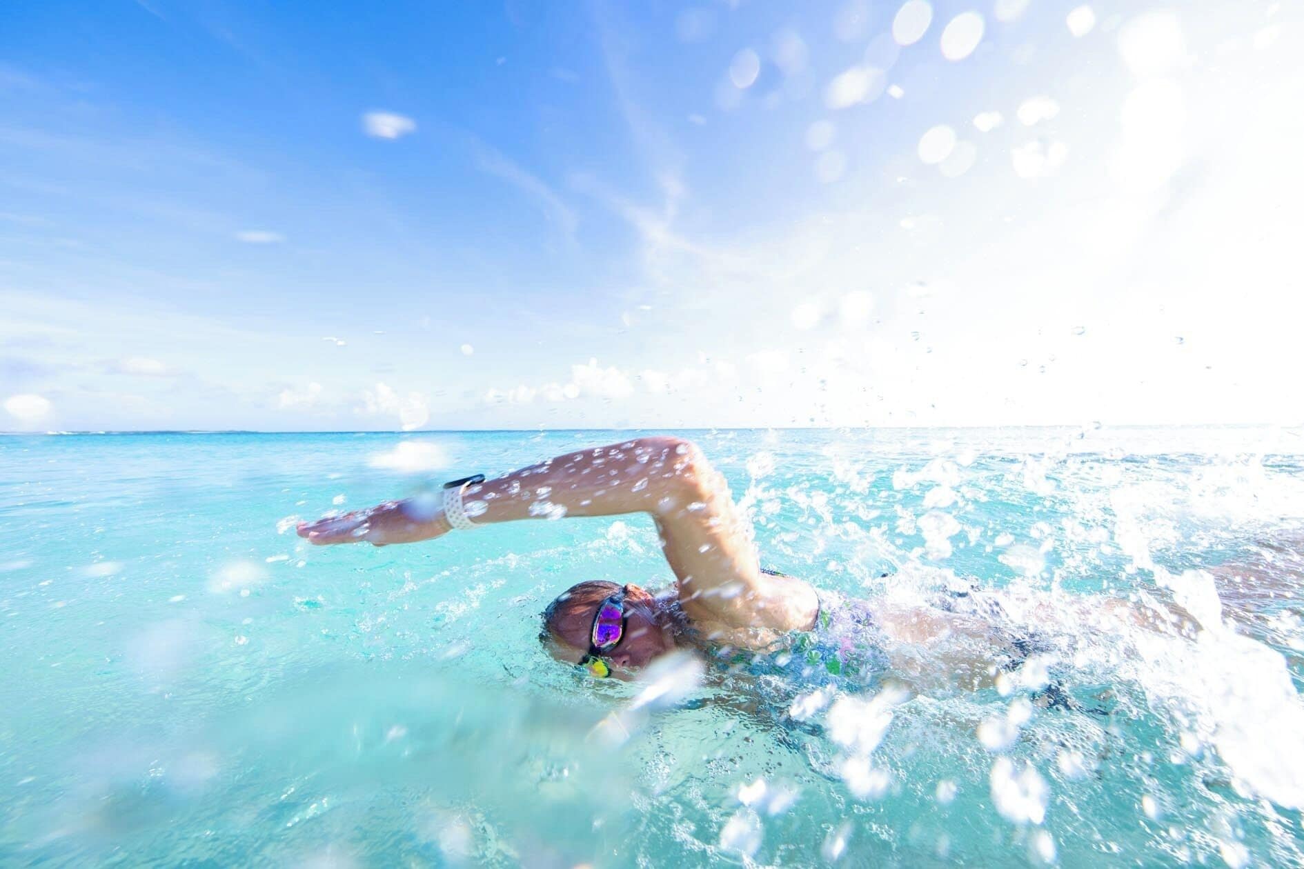 A person swimming in clear blue water with a view of the horizon.