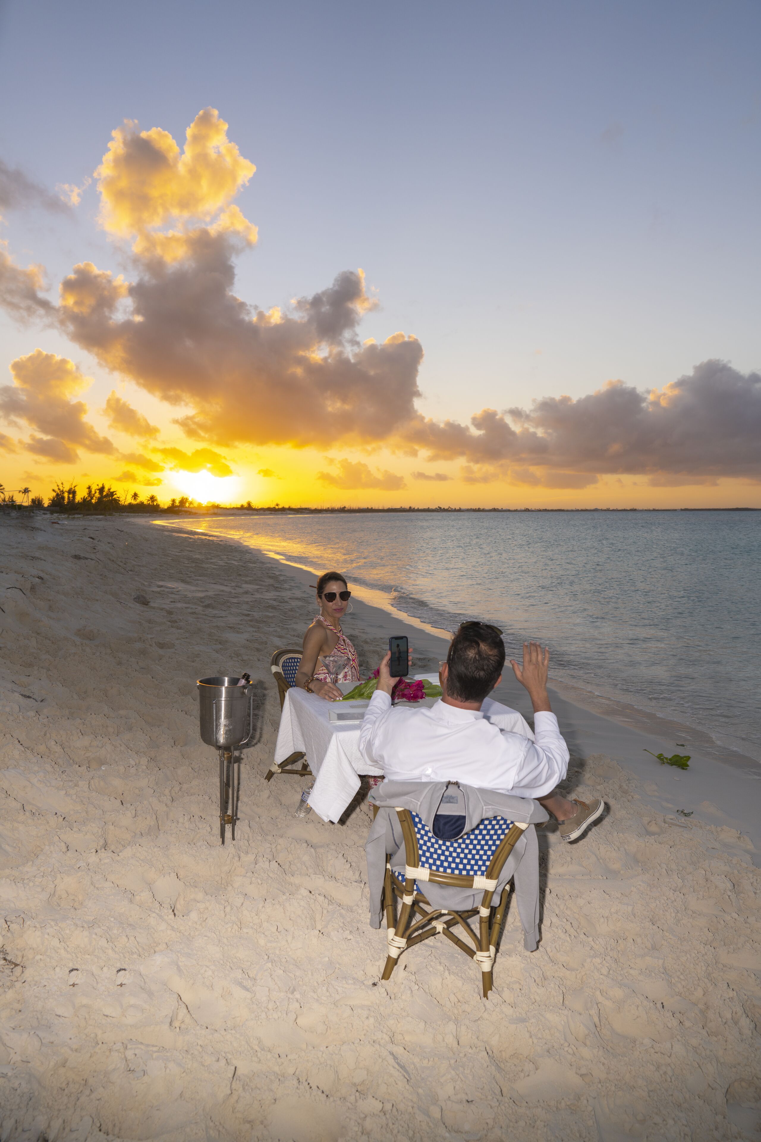 A beachside dining setup with a table, chairs, and a metal bucket.