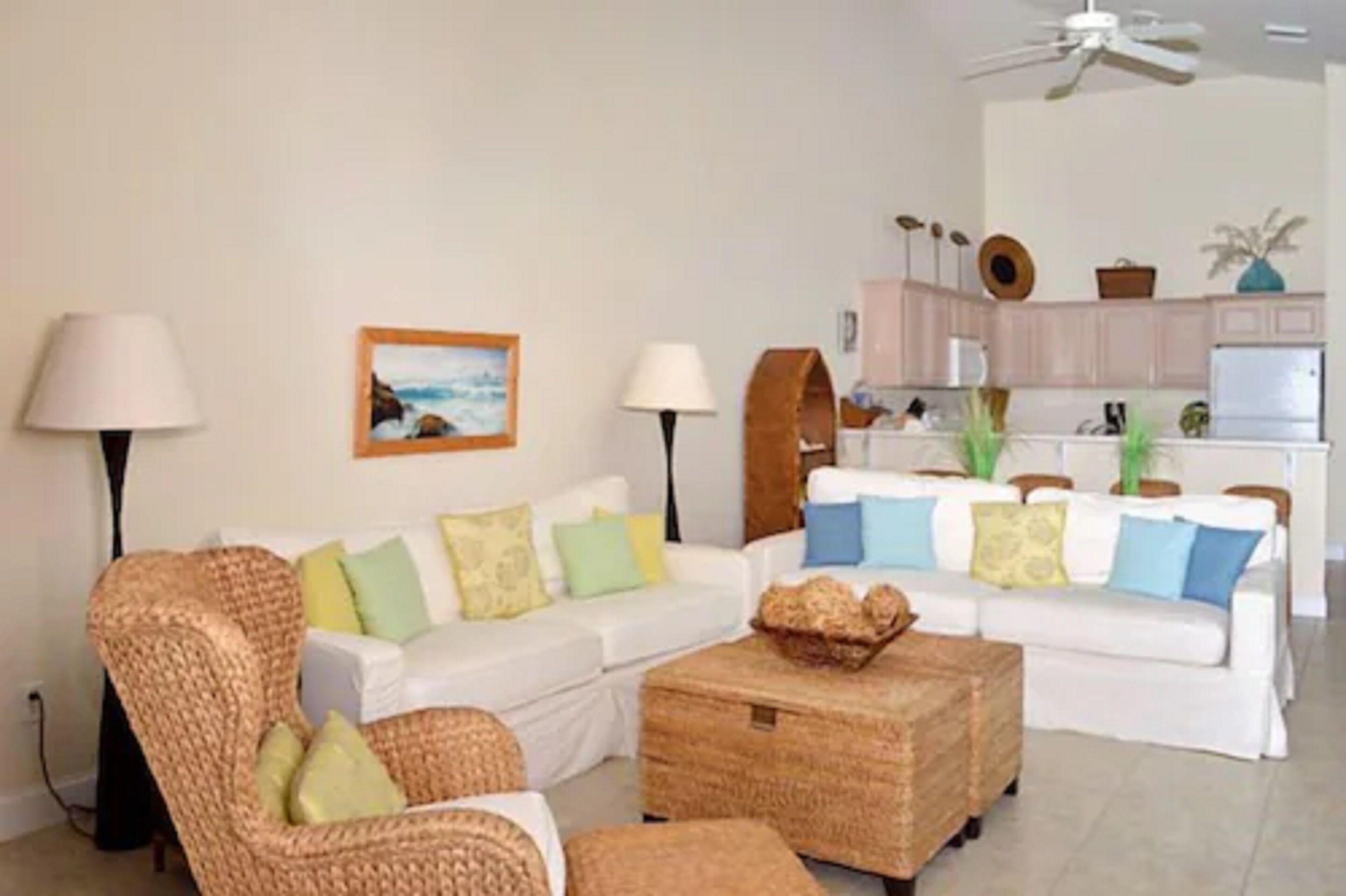 A living room with a sofa set, a wicker chair, a coffee table, and a kitchen in the background.