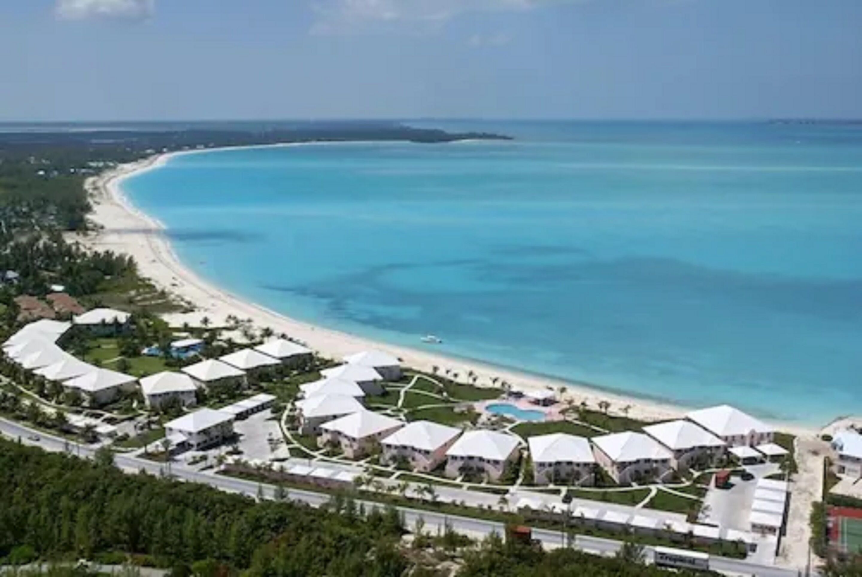 A resort with multiple white-roofed buildings, a beach, and a clear blue sea.