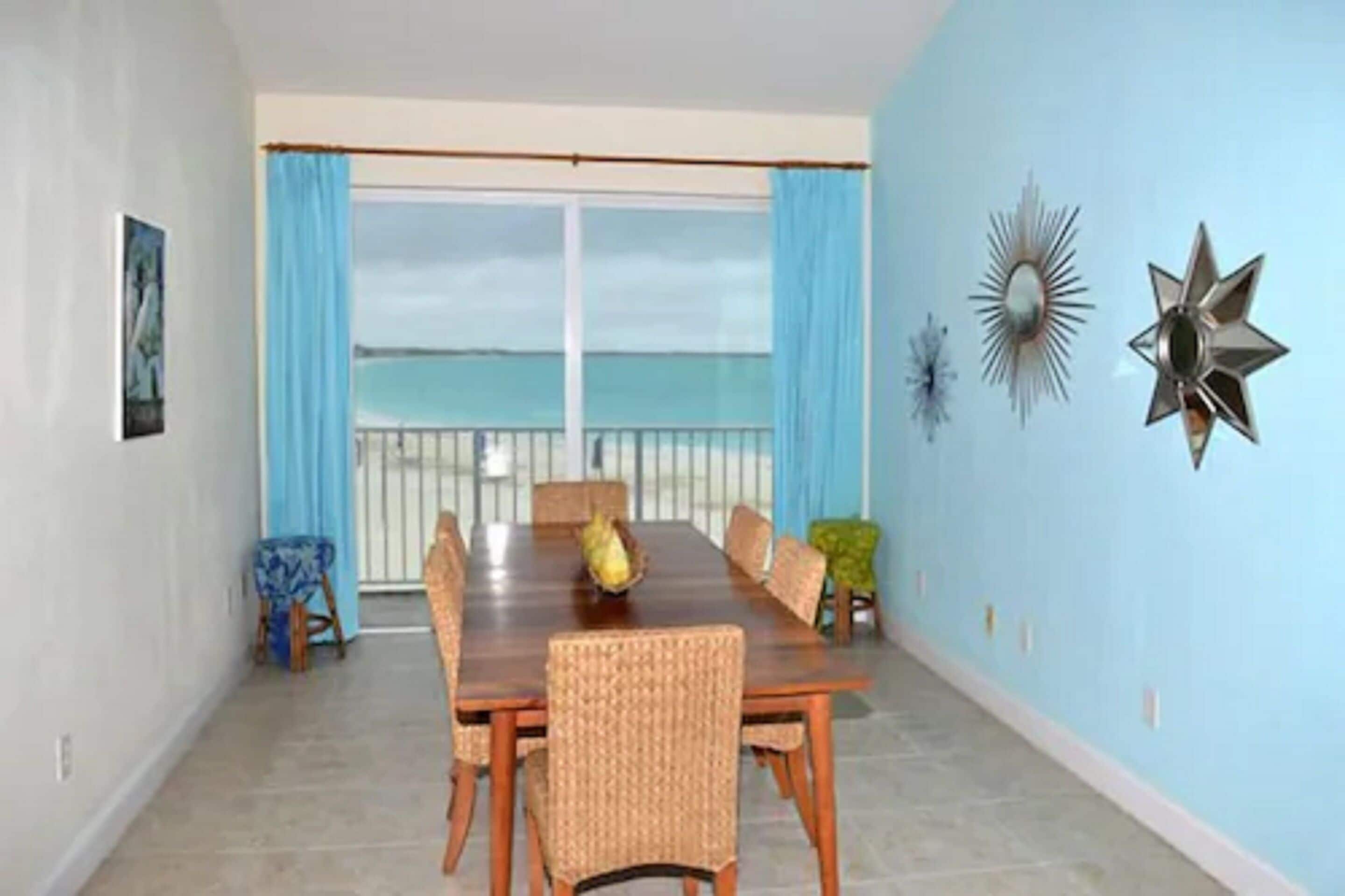 A dining room with a large table and chairs, a view of the ocean through a balcony, and decorative wall art.