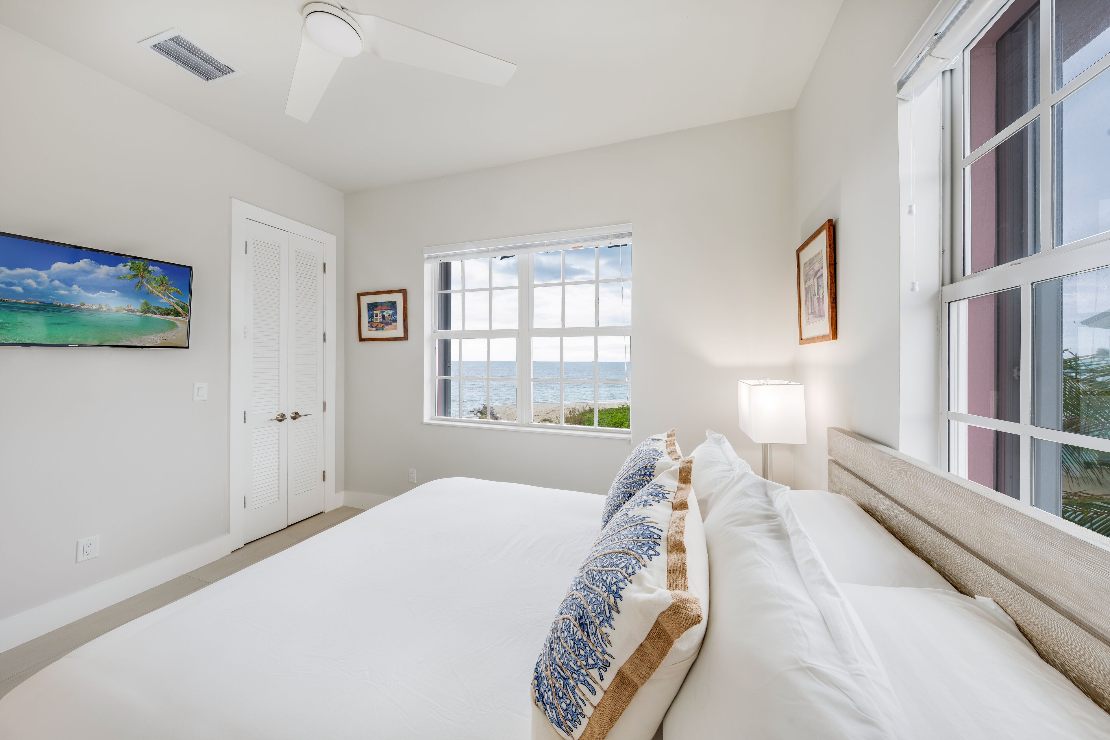 A bedroom with a large bed, a window with a view, a ceiling fan, and a door.