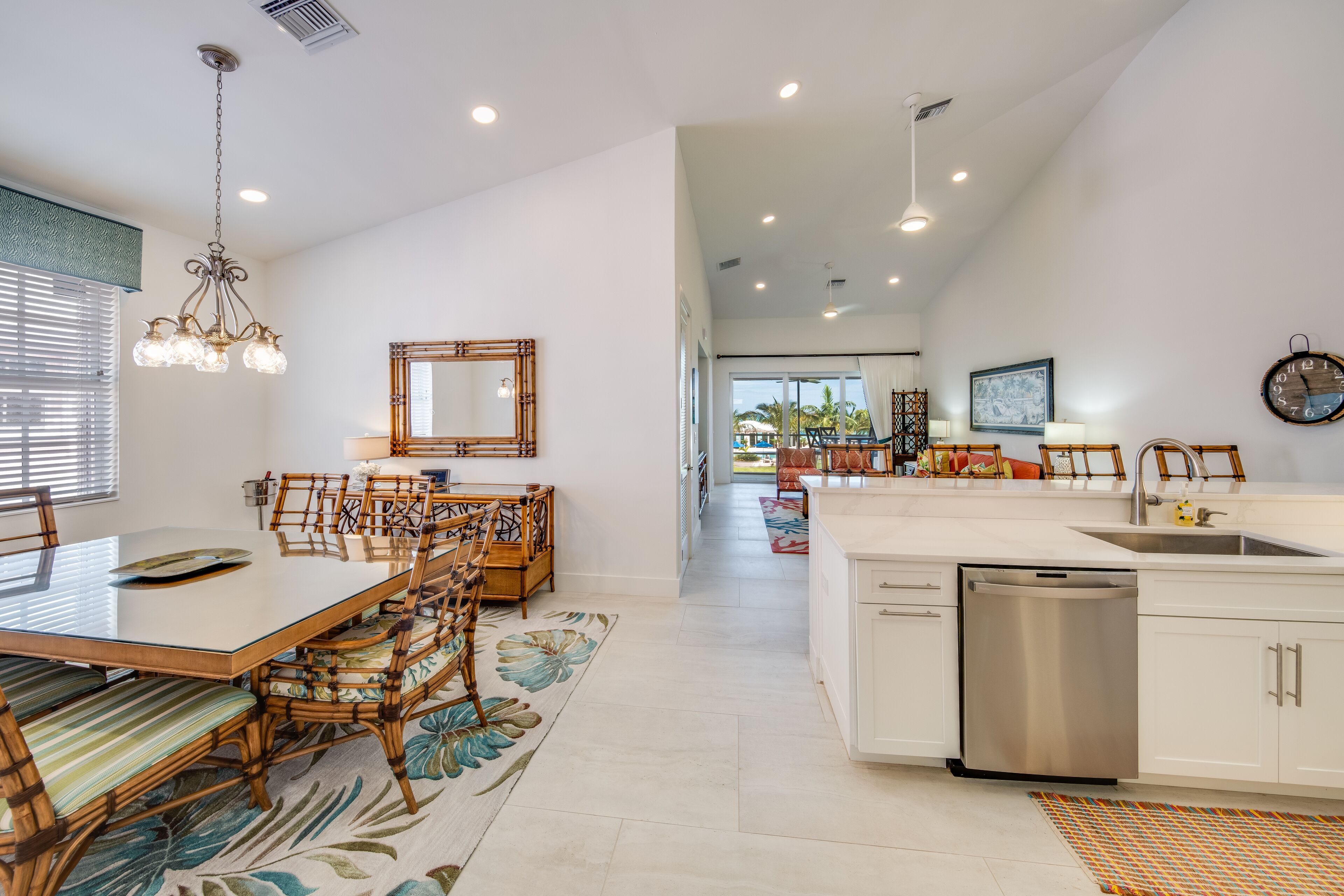 A modern kitchen with white cabinets, a stainless steel dishwasher, and a dining area with a glass table and wooden chairs.