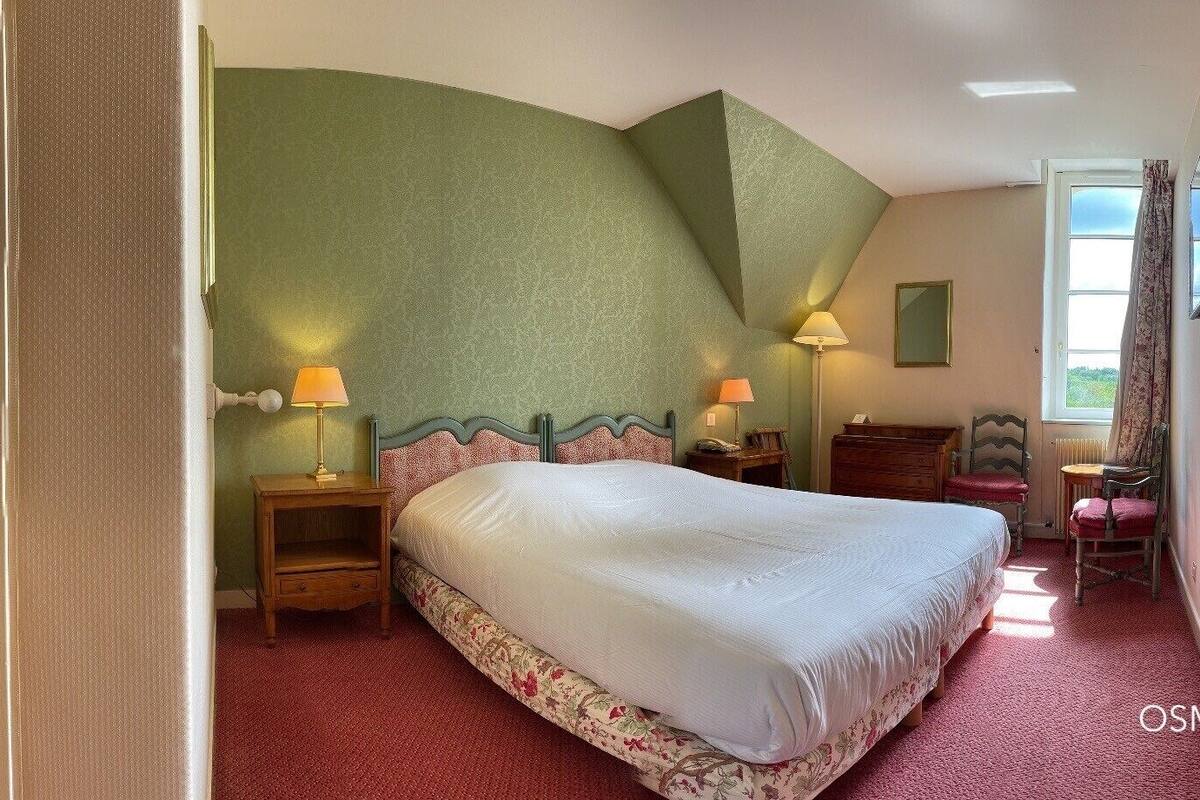 A bedroom with a large bed, a bedside table with a lamp, a nightstand, a chair, and a window with curtains.