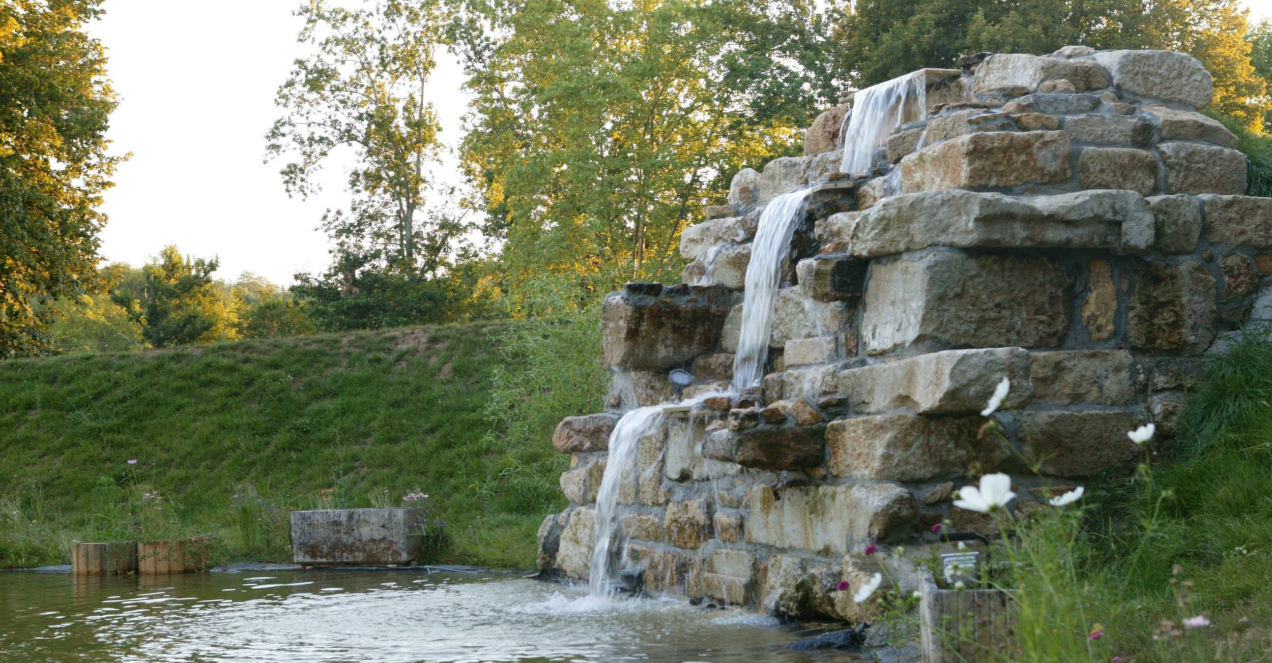 Une cascade de pierres se déversant dans un bassin entouré de verdure.