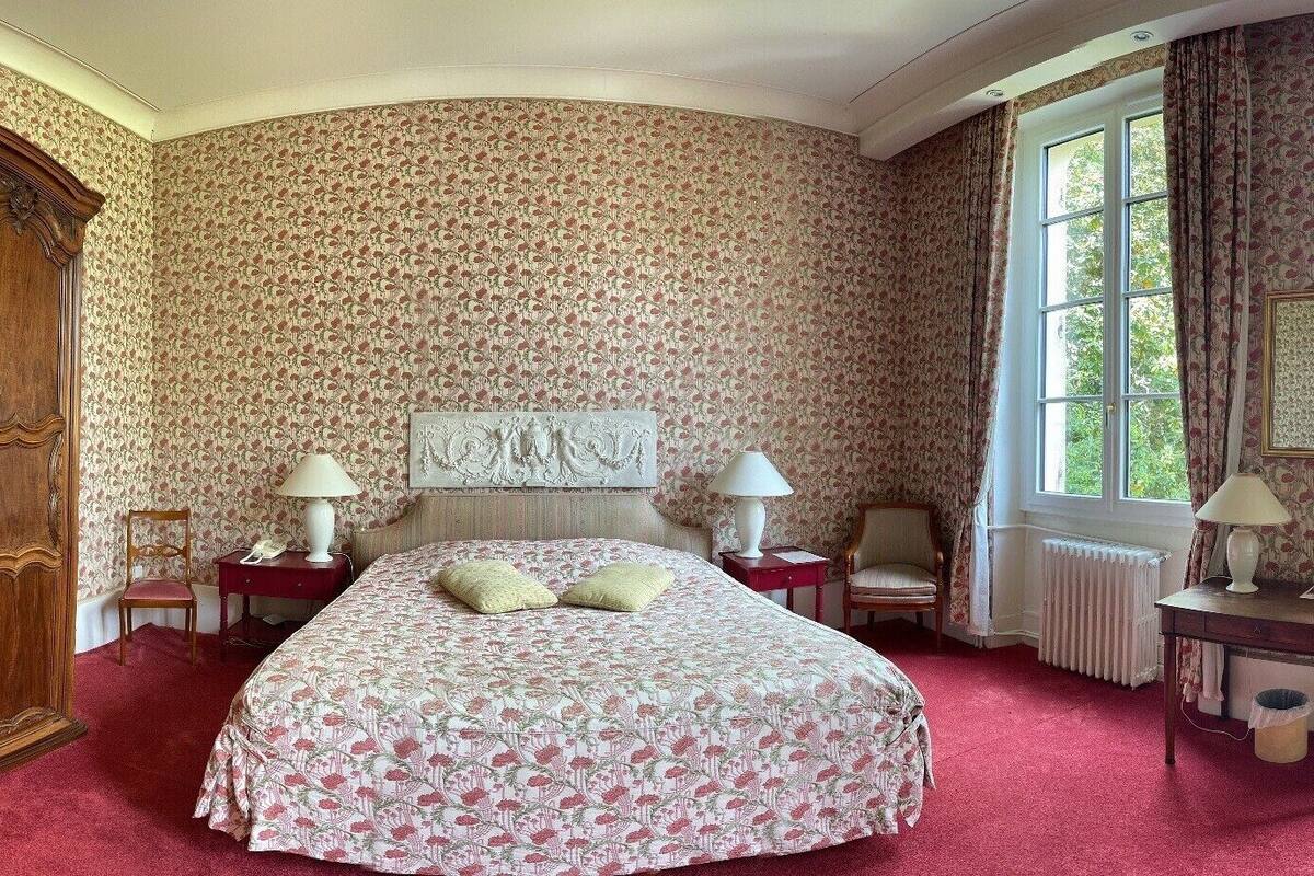 A room with a large bed, a wardrobe, a chair, and a window with curtains.
