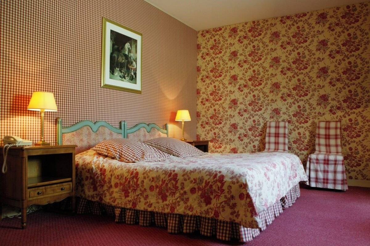 A bedroom with a bed, two bedside lamps, a nightstand, a chair, and a wall with floral wallpaper.