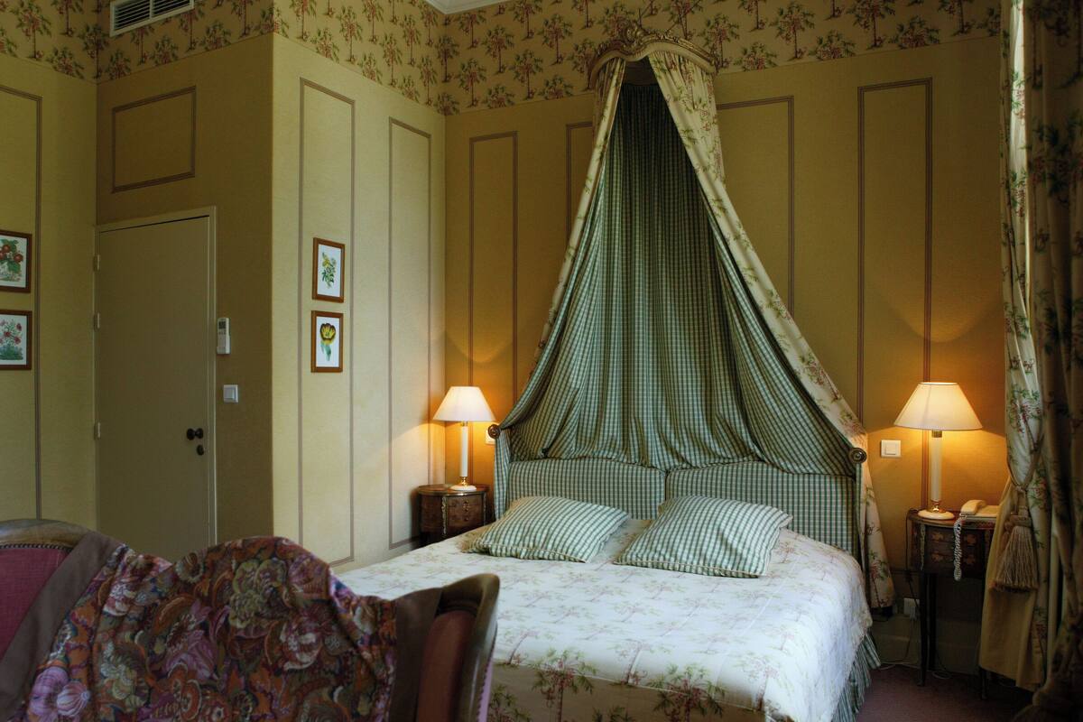 A bedroom with a canopy bed, two bedside lamps, a chair, and a door.