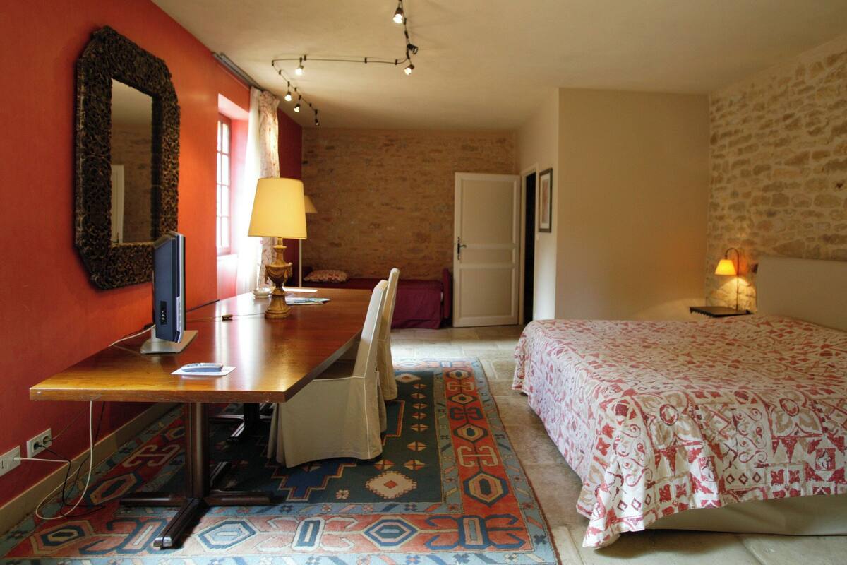 A bedroom with a bed, a desk, a chair, a lamp, and a mirror.