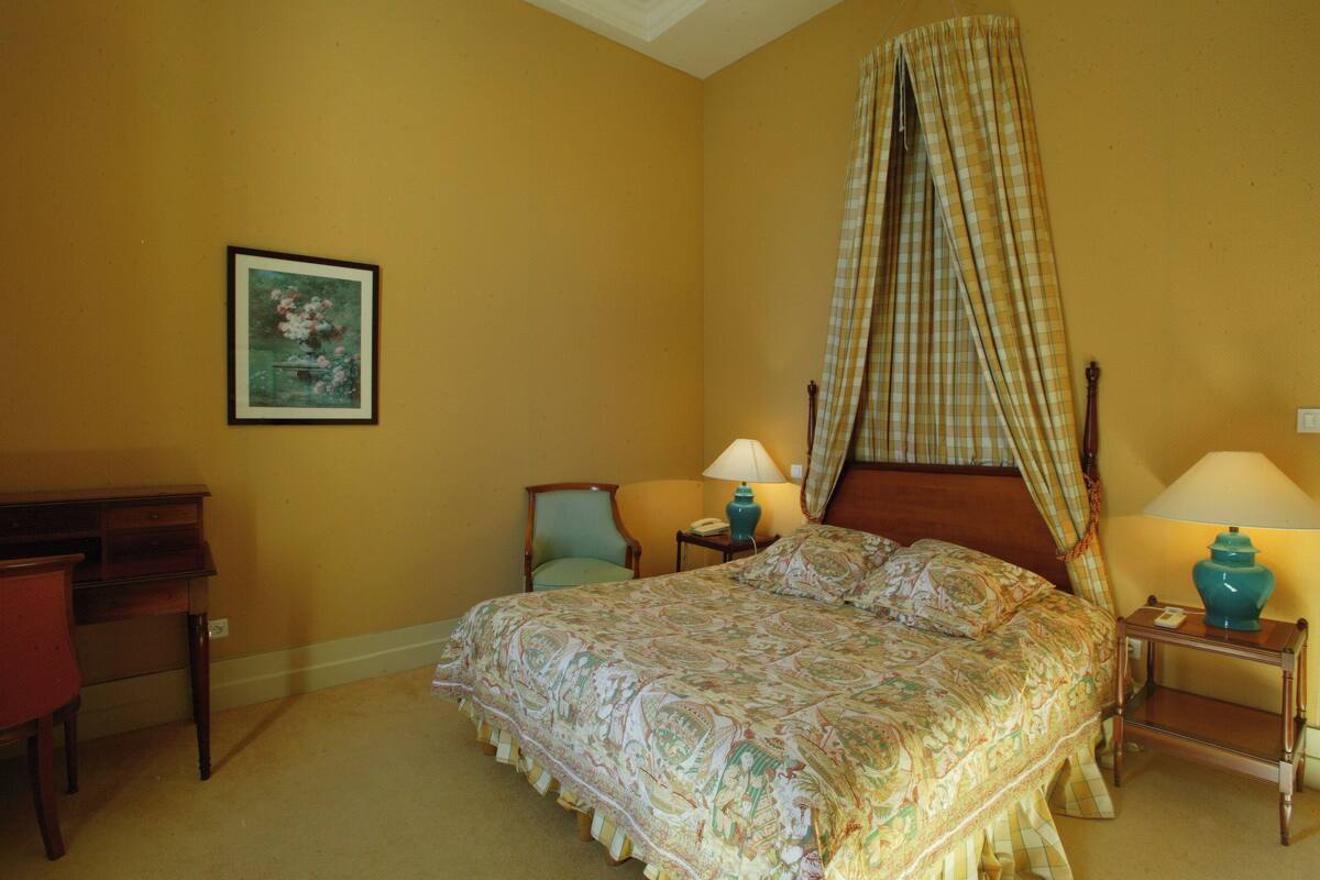A bedroom with a bed, two bedside tables, a chair, a desk, and a painting on the wall.