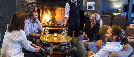 A group of people seated around a table with glasses, in a room with a stone wall and a fireplace.