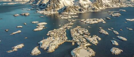 An aerial view of a coastal area with rugged mountains, ice formations, and scattered buildings along the shoreline.