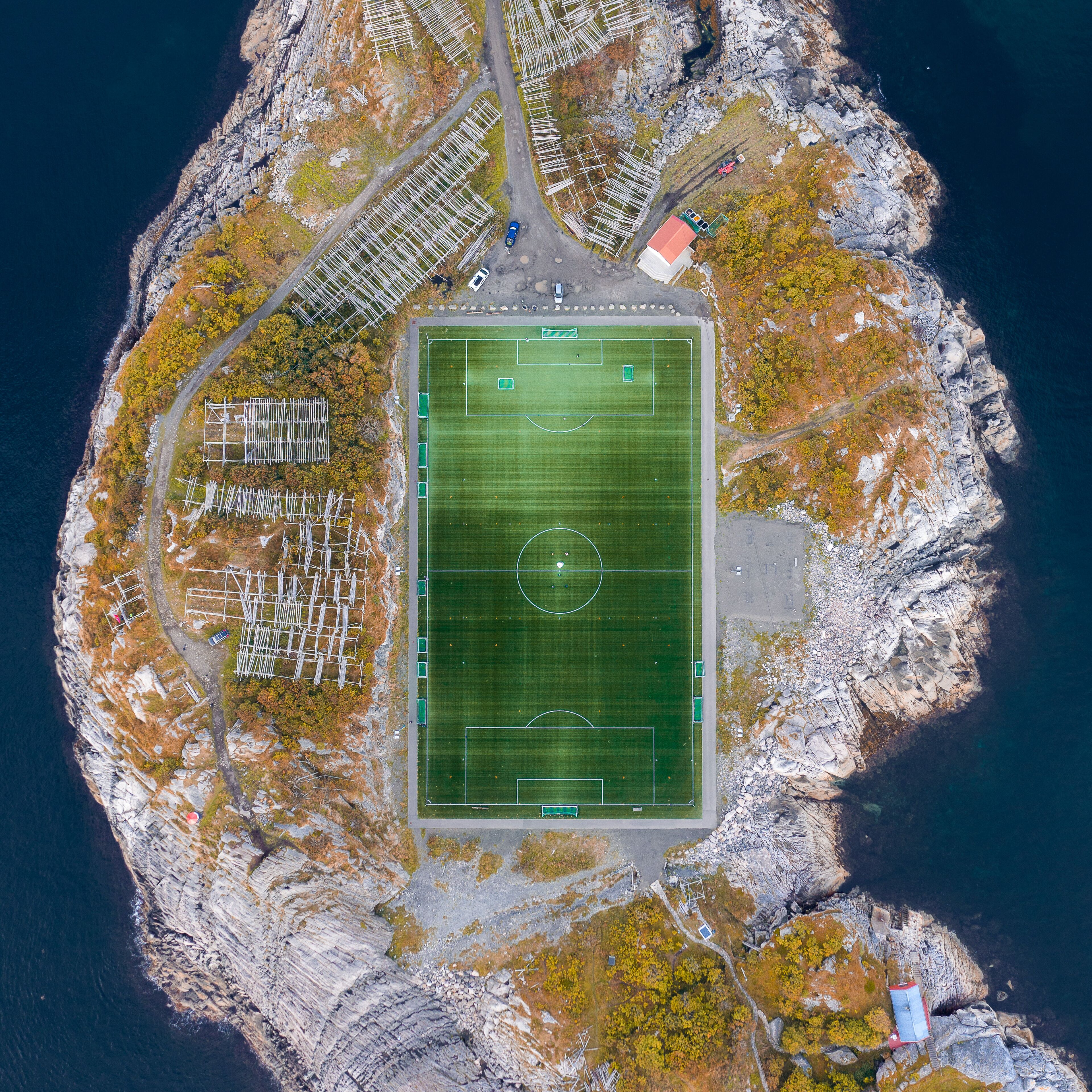 Eine Vogelperspektive zeigt ein Küstenanwesen mit großem Sportplatz, Parkbereich und umgebendem felsigem Gelände.