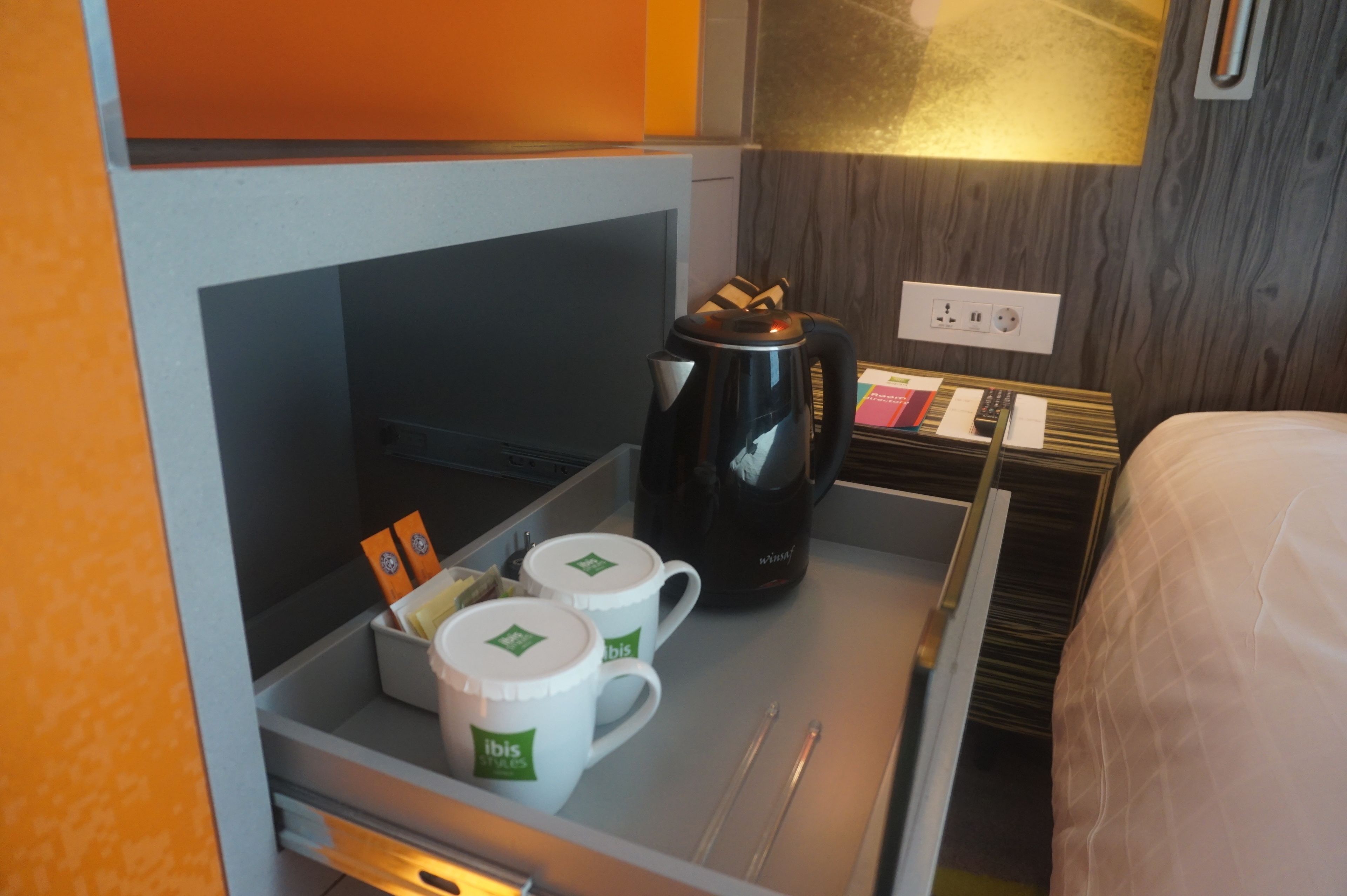 Ein Hotelzimmer mit Minibar, einer Kaffeemaschine und einem Tablett mit einem Buch und einer Fernbedienung.