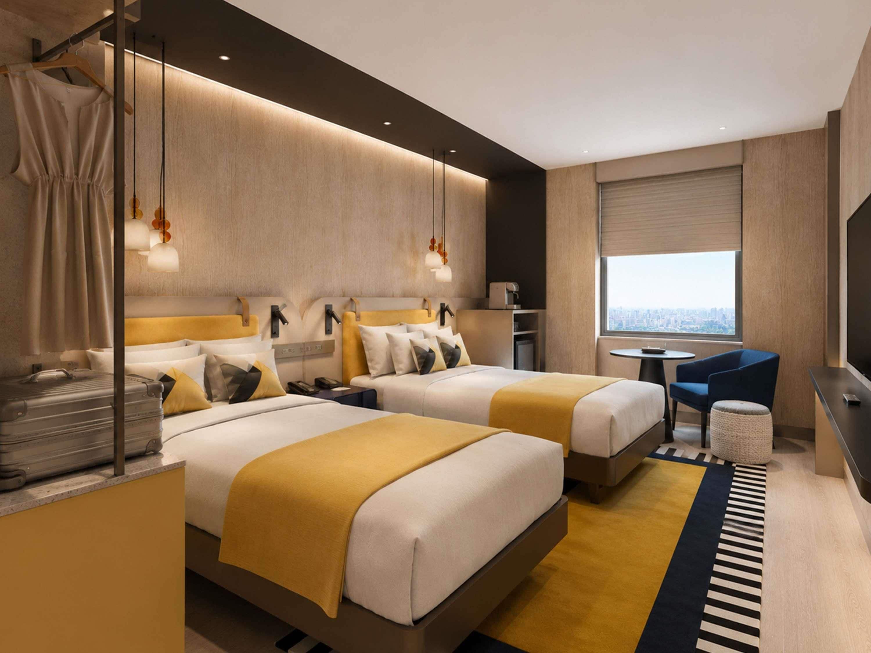 Ein modernes Hotelzimmer mit zwei Betten, einem Schreibtisch, einem Stuhl, einem kleinen Tisch und Blick auf die Stadt.