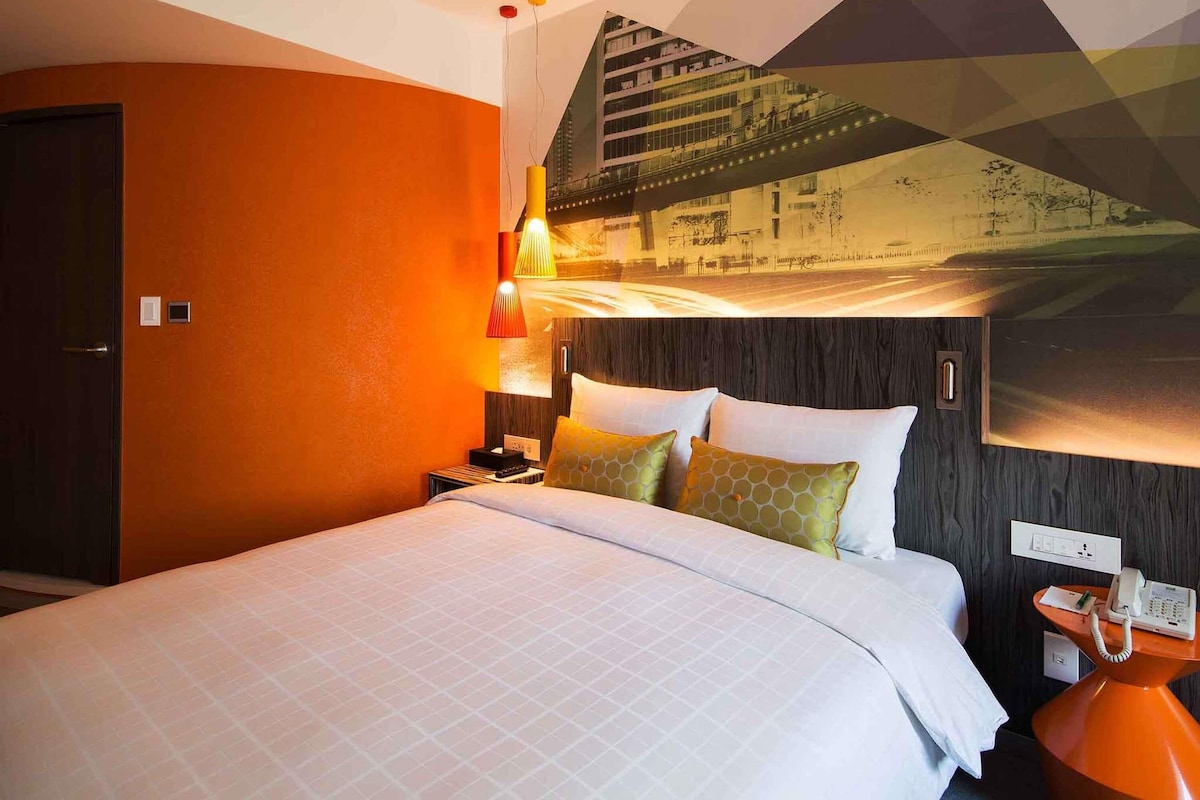 Ein Hotelzimmer mit Bett, Nachttisch, Telefon und einem an der Wand hängenden Kunstwerk.