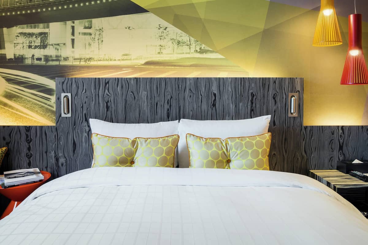 A hotel room with a large bed, a wall-mounted TV, and a bookshelf.