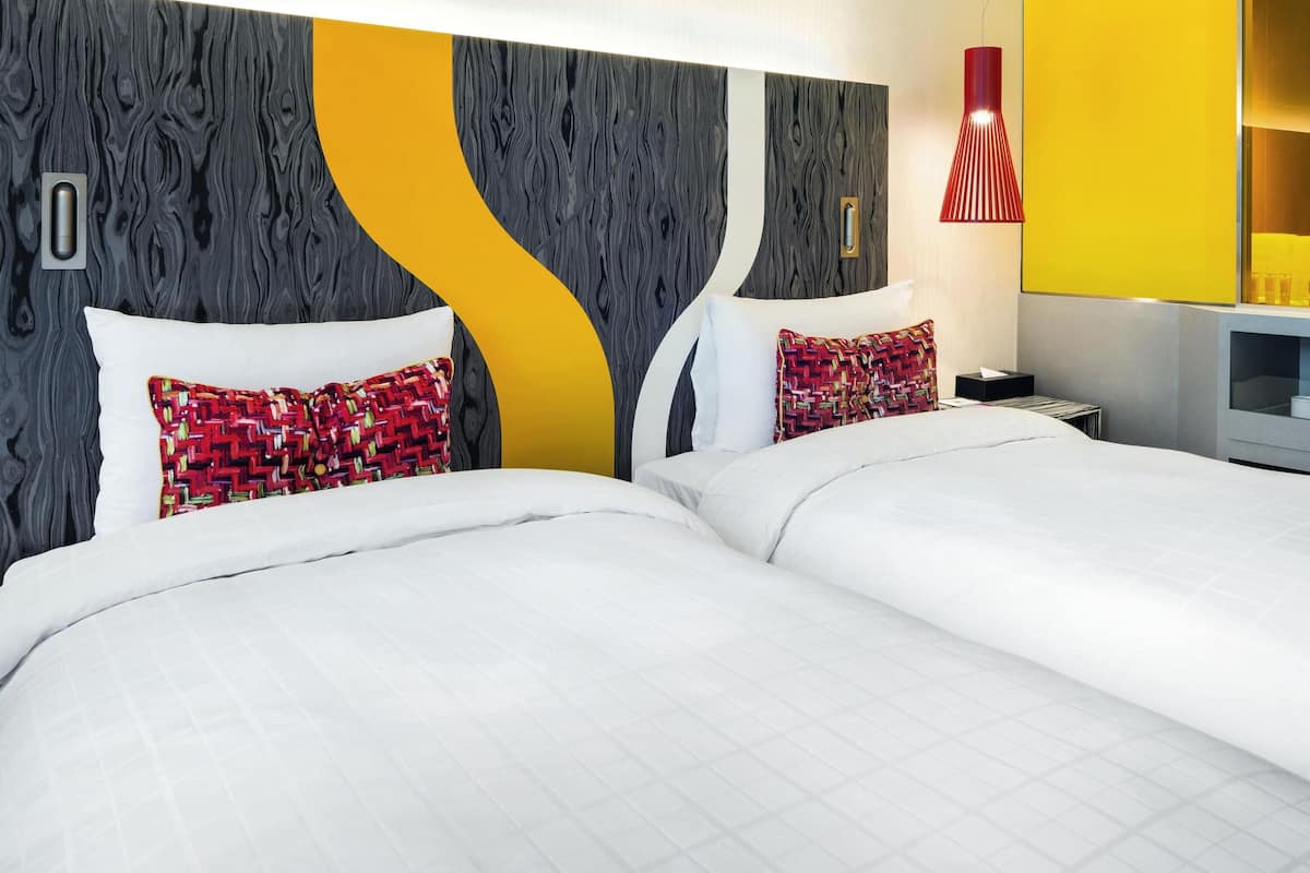 Une chambre d’hôtel moderne avec un grand lit, deux oreillers, une table de chevet et une lampe rouge.