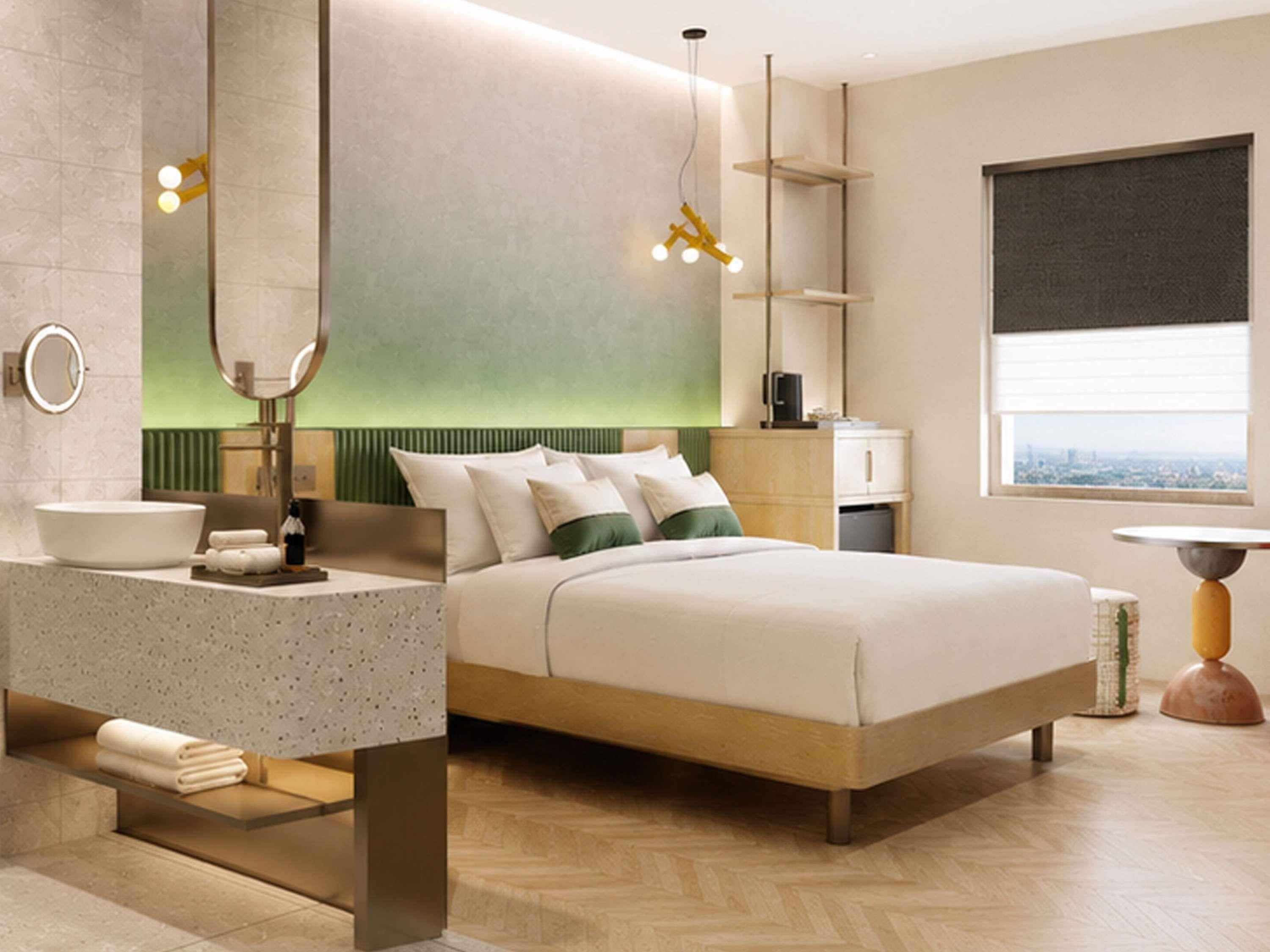 A modern hotel room with a large bed, a bathroom with a round mirror, a sink, and a window with a city view.