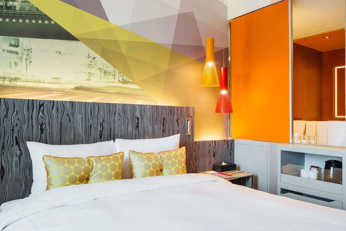 Ein Hotelzimmer mit Bett, Nachttisch, Lampe und einem großen Spiegel.