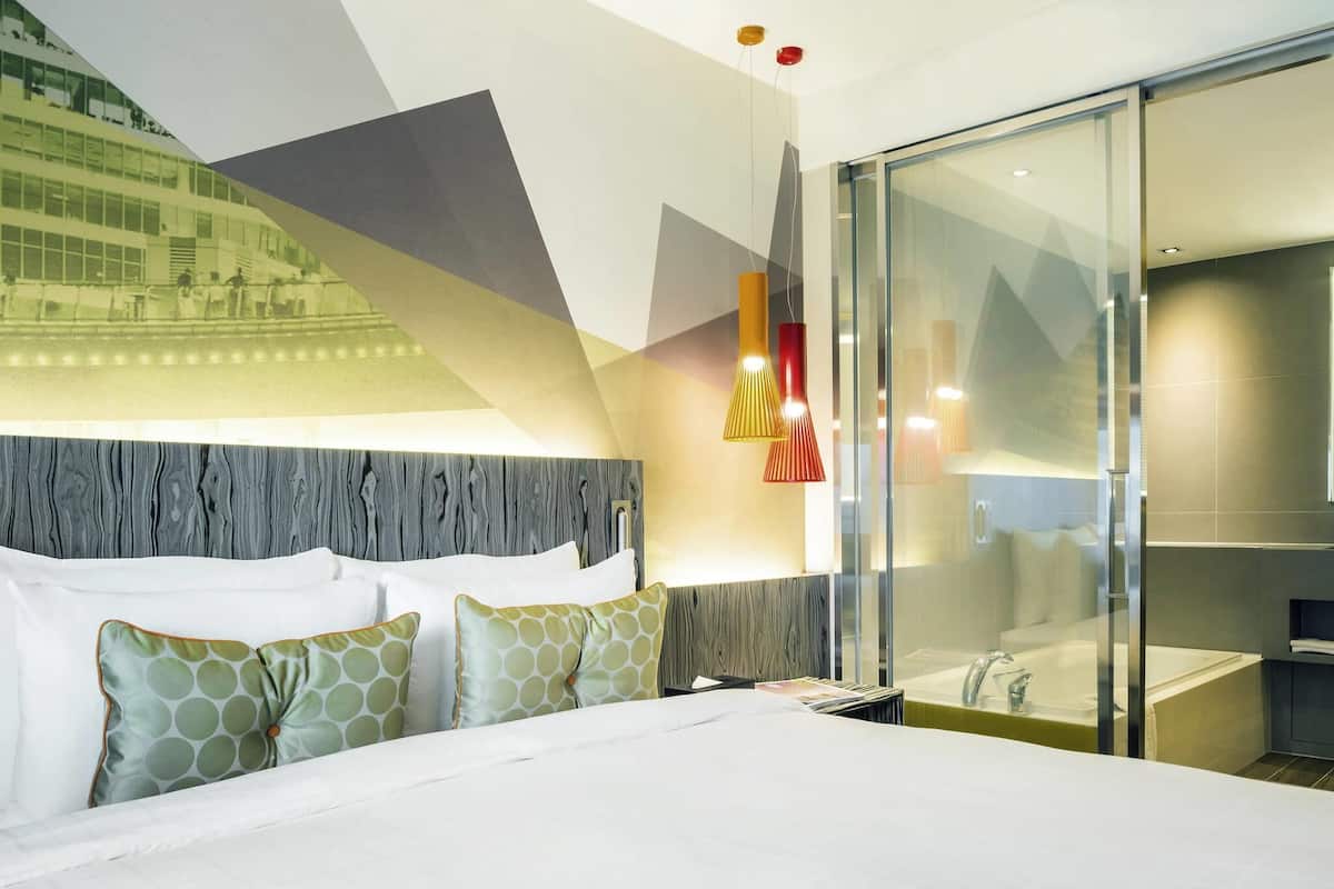 Une chambre d’hôtel moderne avec un grand lit, une douche en verre et une vue sur un bâtiment à l’extérieur.