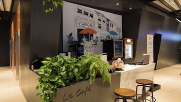 Un comptoir de café avec une enseigne indiquant « Le Café », une machine à café, un tableau affichant le menu et deux tabourets.